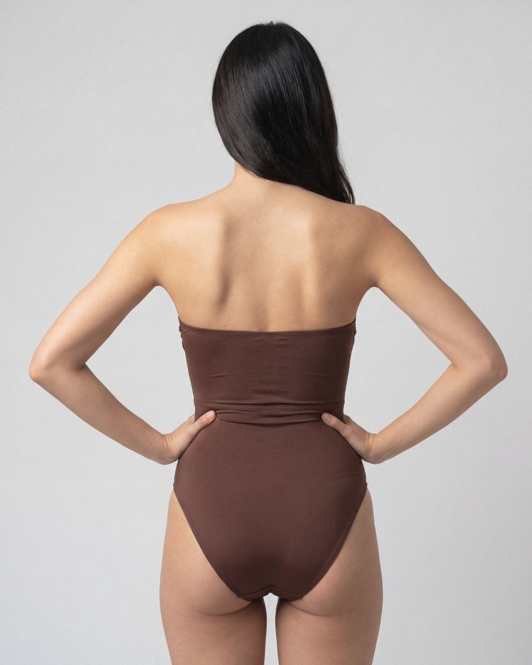 Woman wearing a brown strapless swimsuit against a gray background