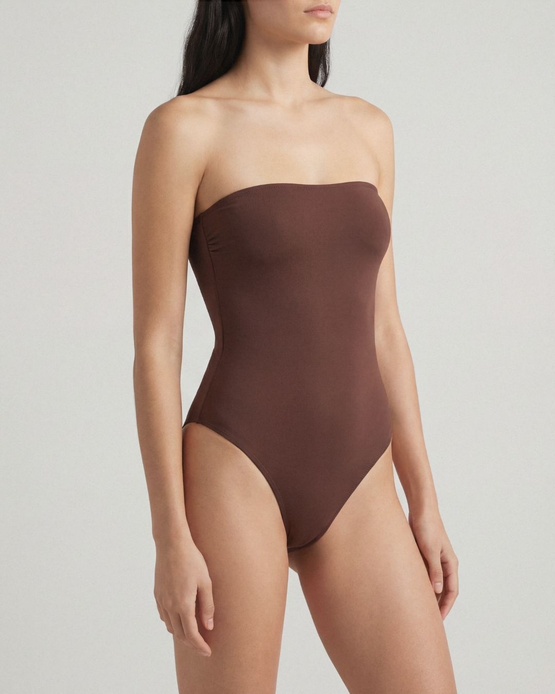 Brown strapless swimsuit worn by a model on a light gray background