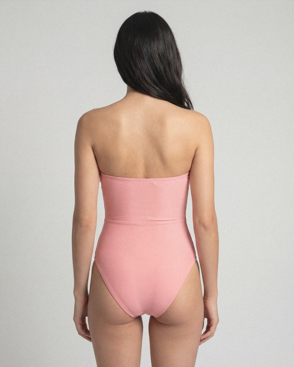 Person wearing a pink strapless swimsuit against a gray background