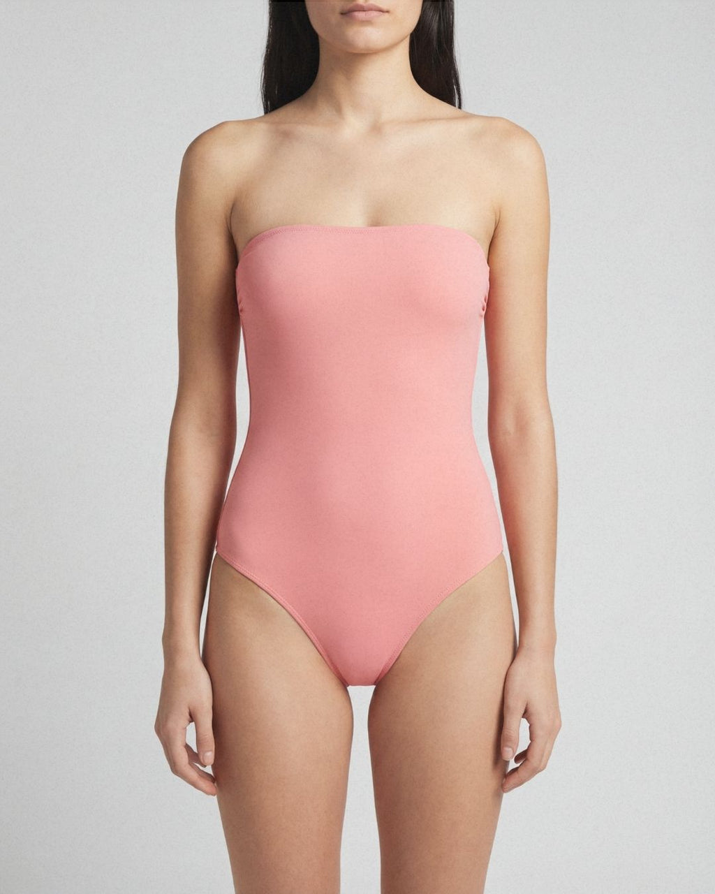 Woman wearing a pink strapless swimsuit against a plain background