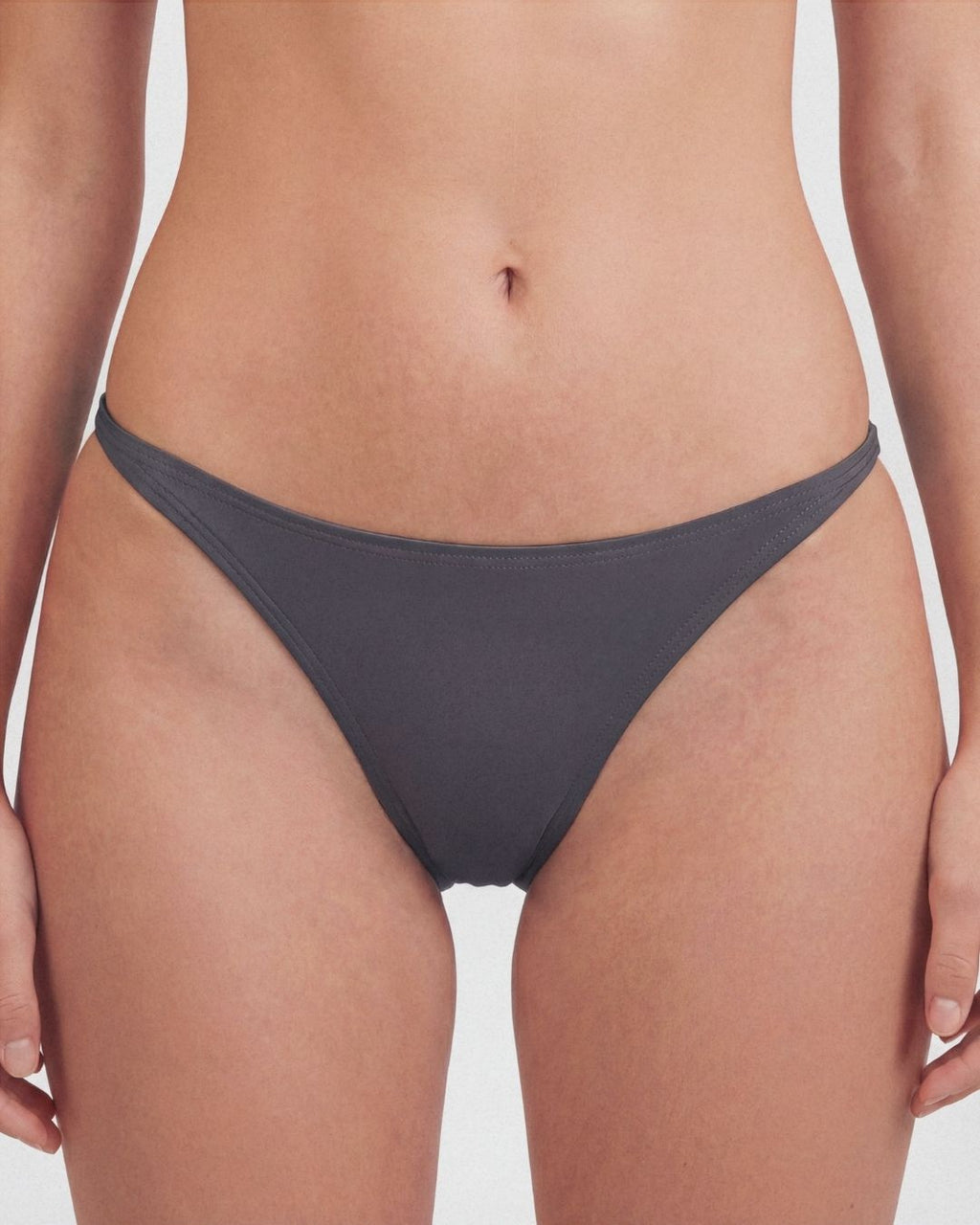 Person wearing dark gray bikini bottoms on a plain background