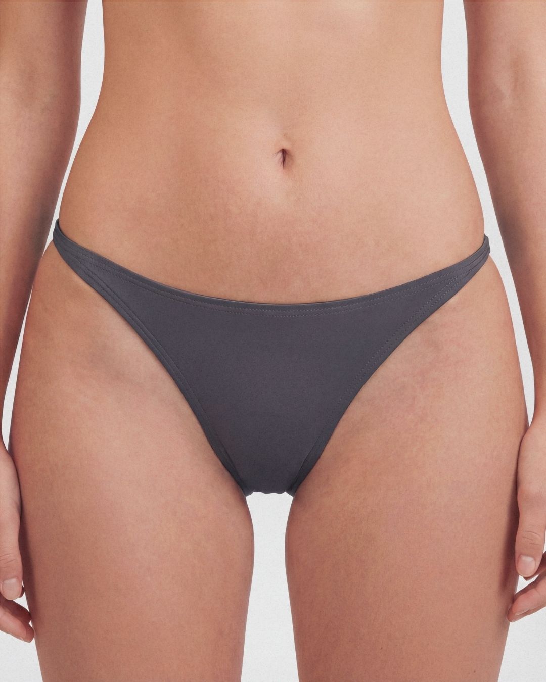 Person wearing dark gray bikini bottoms on a plain background