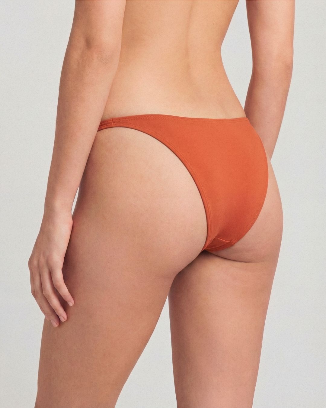 Orange bikini bottom worn by a person on a plain background
