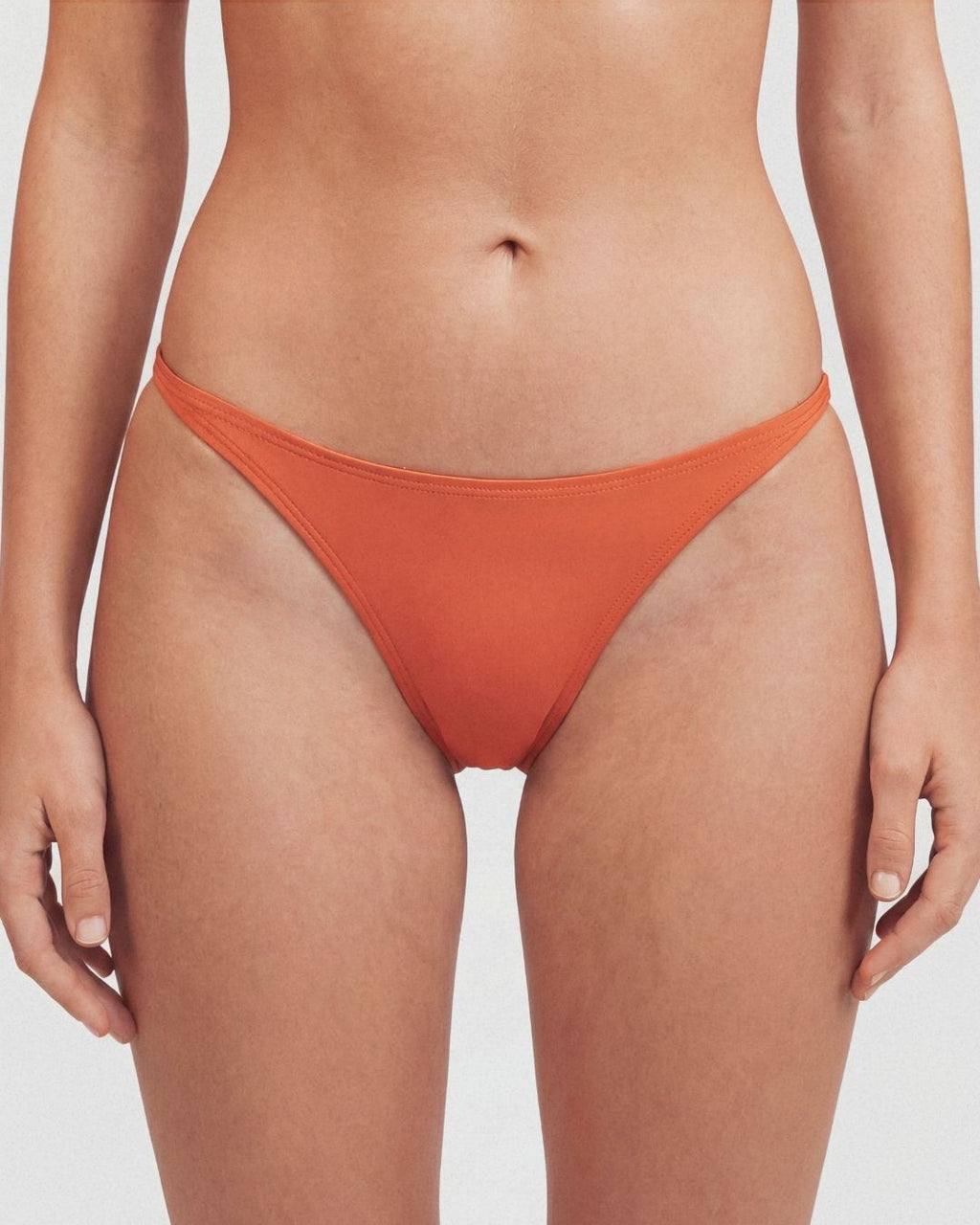 Person wearing orange bikini bottoms on a plain background