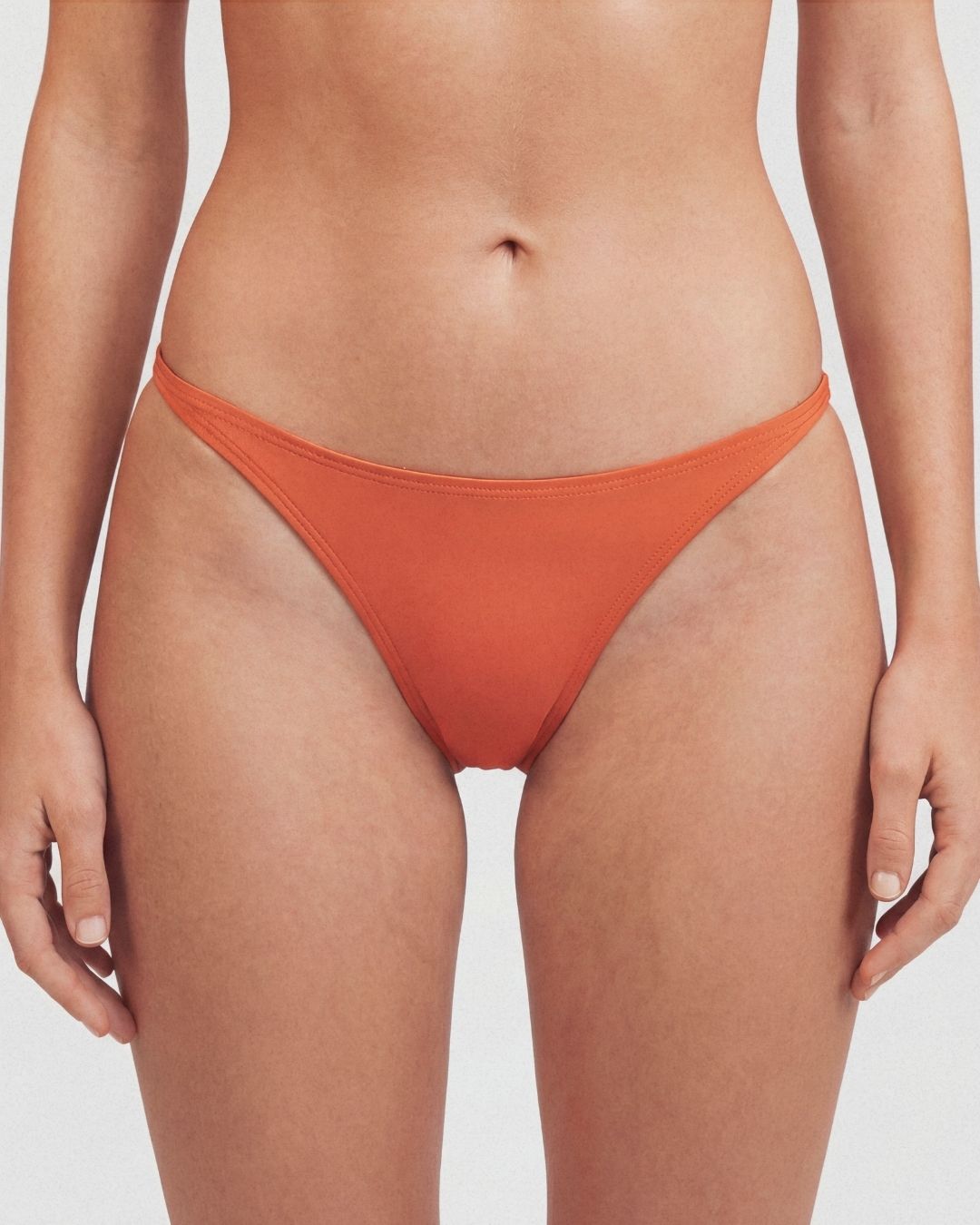 Person wearing orange bikini bottoms on a plain background