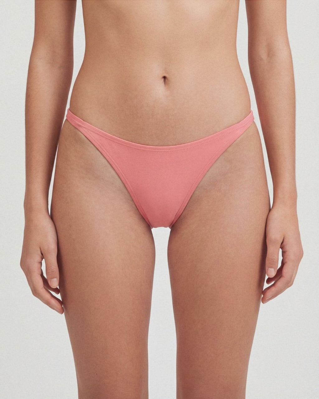 Person wearing a coral pink bikini bottom on a plain background