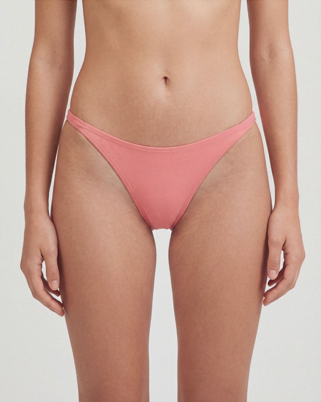 Person wearing a coral pink bikini bottom on a plain background