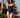 Woman in a navy swimsuit holding a navy cover-up on a track with palm trees in the background