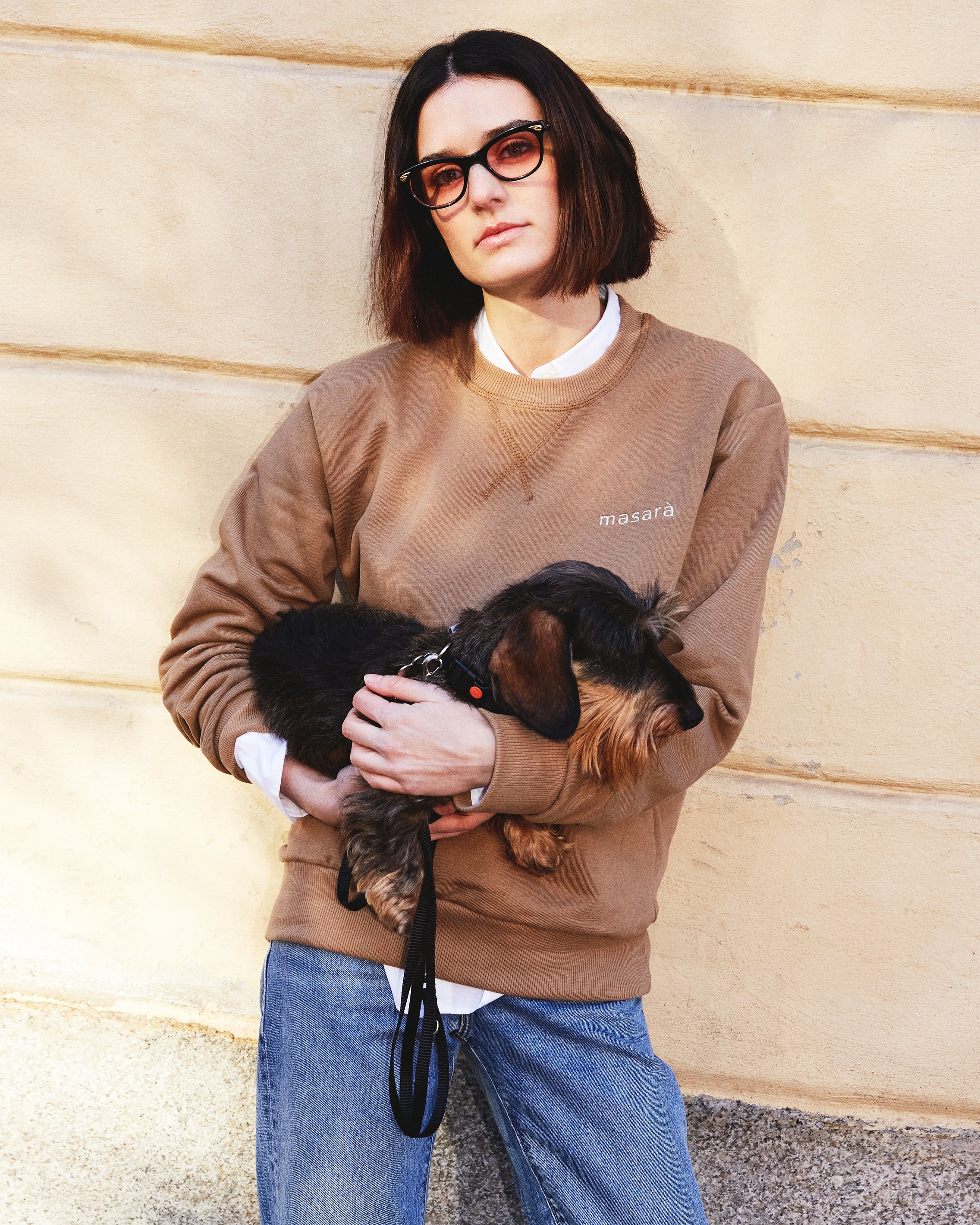 Girl wearing masara cacao sweatshirt and holding small dog 