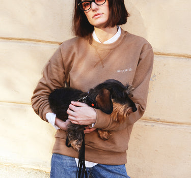 Girl wearing masara cacao sweatshirt and holding small dog 