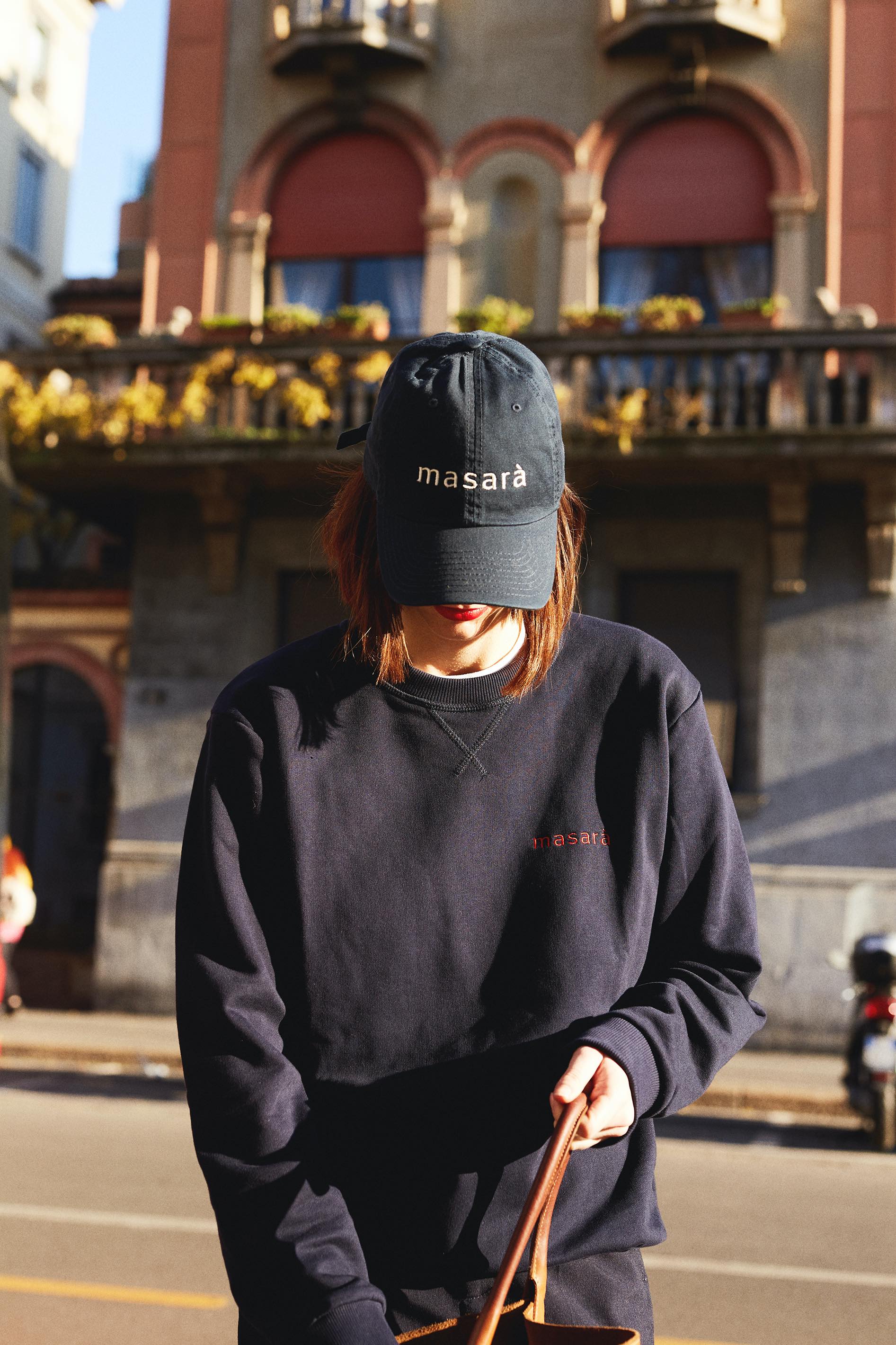 Girl on the street looking inside her bag and wearing masara navy blue dad hat and sweatshirt