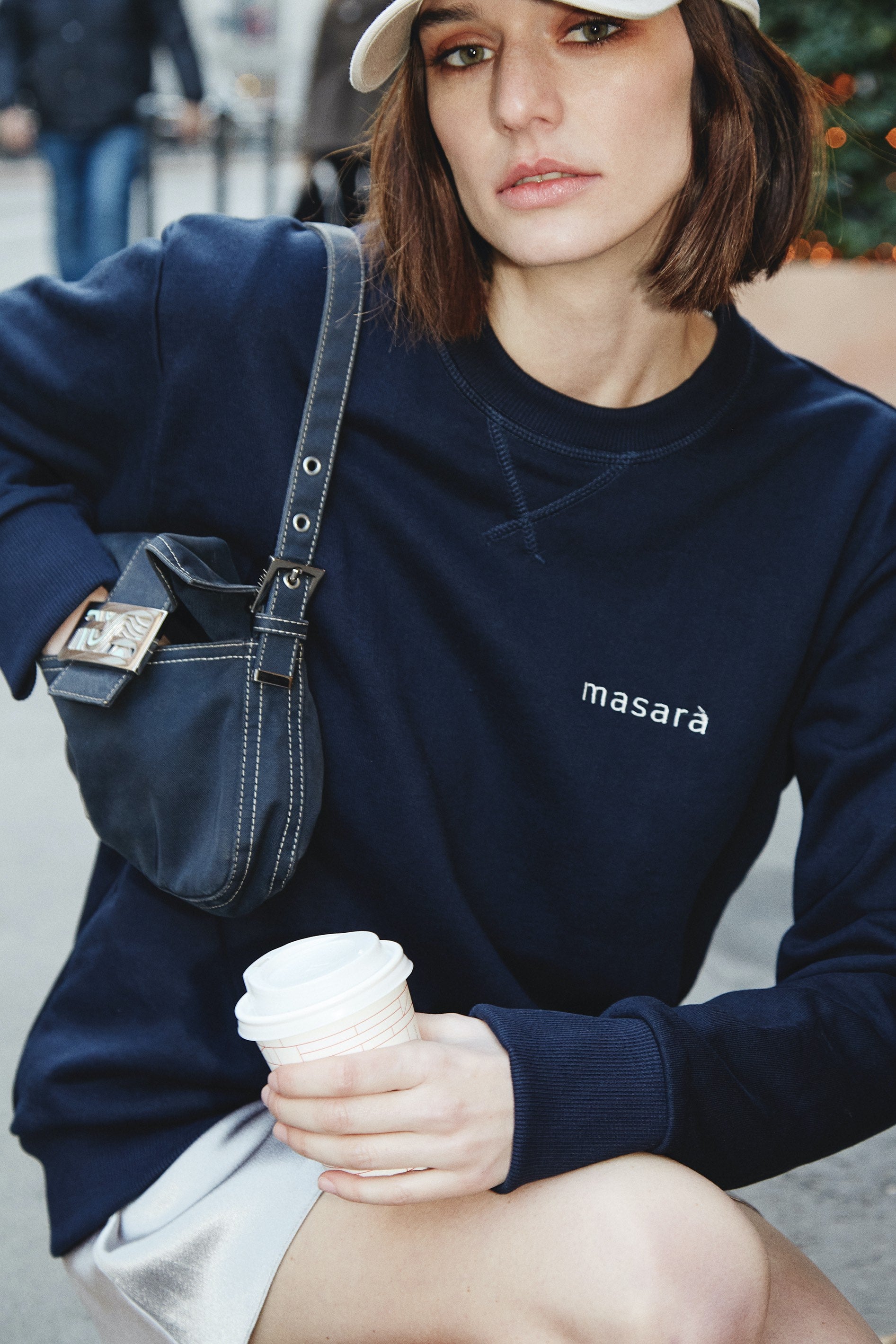 Girl on the street holding her coffee wearing masara navy blue and cream logo sweatshirt