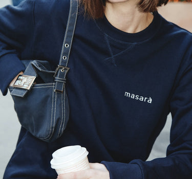 Girl on the street holding her coffee wearing masara navy blue and cream logo sweatshirt