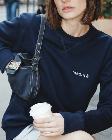 Girl on the street holding her coffee wearing masara navy blue and cream logo sweatshirt