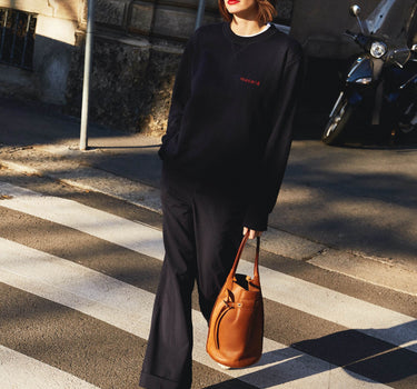 Girl crossing the street wearing masara navy blue and red sweatshirt and navy blue hat 