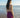 Woman in a purple dress standing on a beach looking at the ocean.