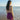Woman in a purple dress standing on a beach looking at the ocean.