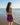 Woman in a purple dress standing on a beach looking at the ocean.