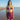Woman in a purple bikini and sarong standing on a beach.