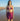 Woman in a purple bikini and sarong standing on a beach.