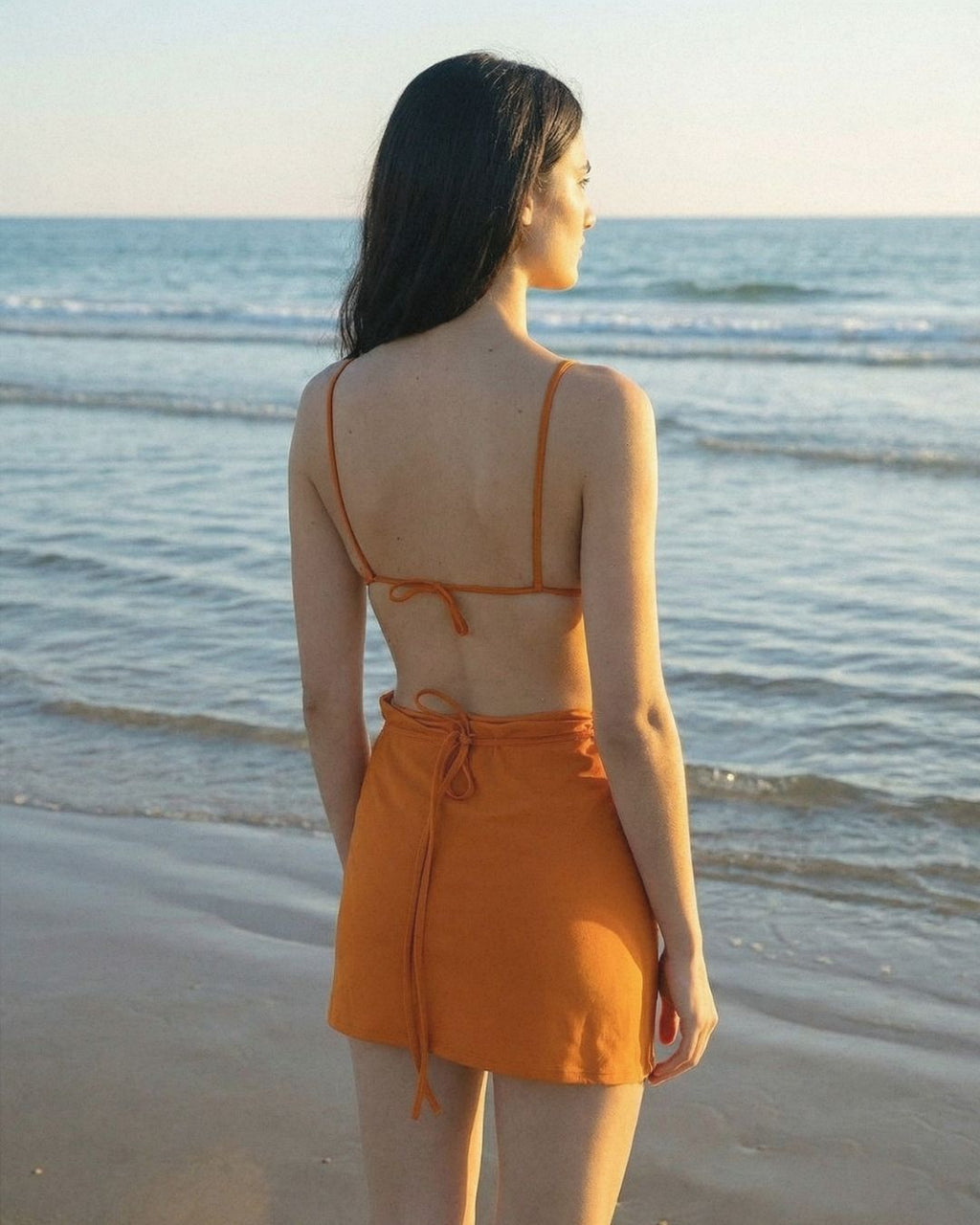 Woman in an orange dress standing on a beach with ocean waves in the background