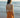 Woman in an orange dress standing on a beach with ocean waves in the background