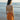 Woman in an orange dress standing on a beach with ocean waves in the background