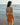 Woman in an orange dress standing on a beach with ocean waves in the background