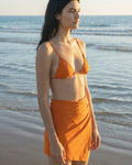 Woman in an orange bikini standing on a beach with ocean in the background
