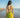 Woman in a yellow bikini standing on a beach with clear blue sky.