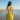 Woman in a yellow bikini standing on a beach with clear blue sky.