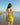 Woman in a yellow bikini standing on a beach with clear blue sky.