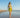 Woman in a yellow bikini and skirt standing on a beach with clear blue sky.