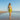 Woman in a yellow bikini and skirt standing on a beach with clear blue sky.