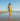 Woman in a yellow bikini and skirt standing on a beach with clear blue sky.