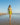 Woman in a yellow bikini and skirt standing on a beach with clear blue sky.