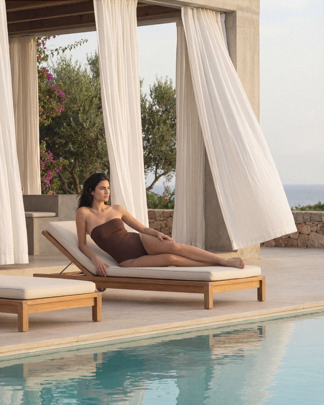 Woman lounging on a sunbed by a pool with curtains in the background