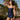 Woman in a navy blue swimsuit standing outdoors with palm trees in the background