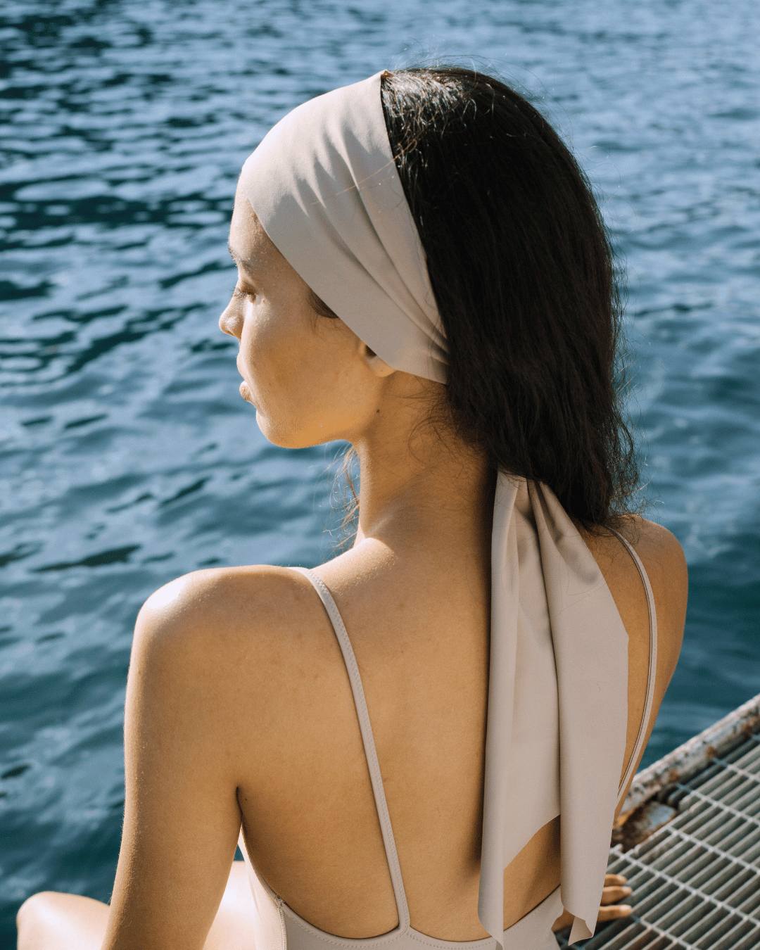 Woman with a beige headscarf sitting by a body of water