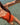 A woman wearing a bright orange one-piece swimsuit floating in clear, sunlit shallow water.