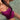 A close-up lifestyle shot of a woman wearing a vibrant magenta one-piece swimsuit while standing in clear, shallow water.