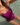 A close-up lifestyle shot of a woman wearing a vibrant magenta one-piece swimsuit while standing in clear, shallow water.