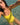 A woman in a bright yellow one-piece swimsuit taking a selfie in clear, shallow turquoise water.