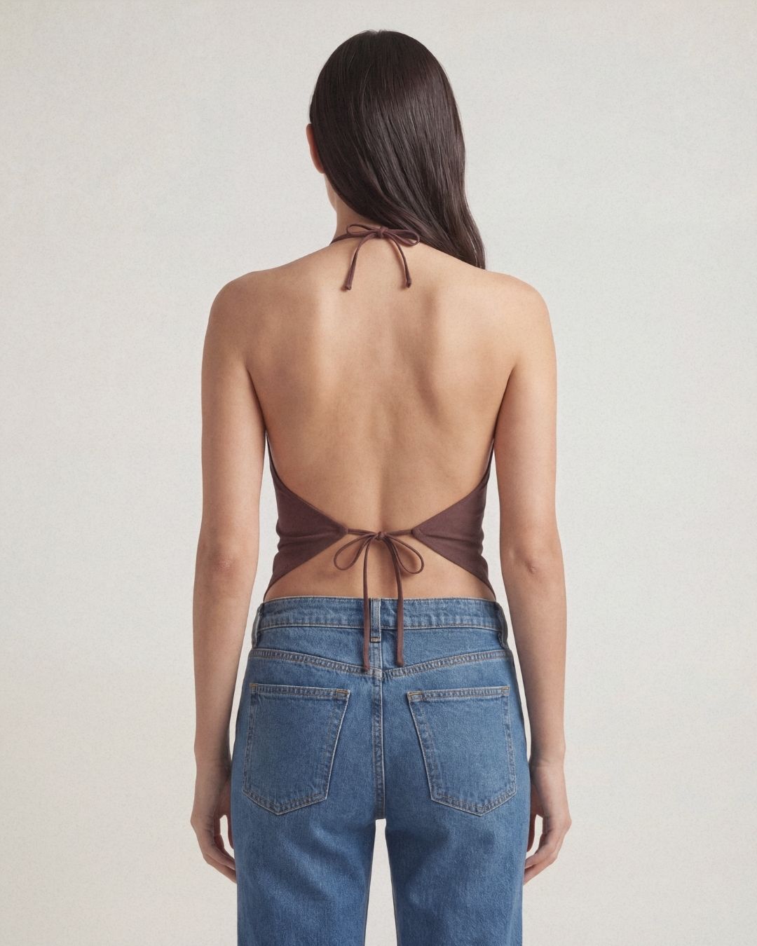 Woman wearing a brown halter top and blue jeans on a plain background