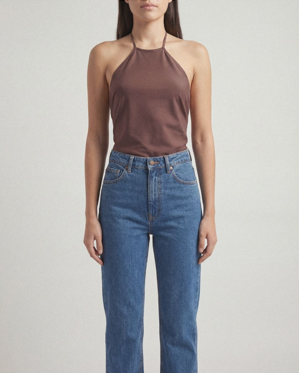 Person wearing a brown halter top and blue jeans on a light gray background