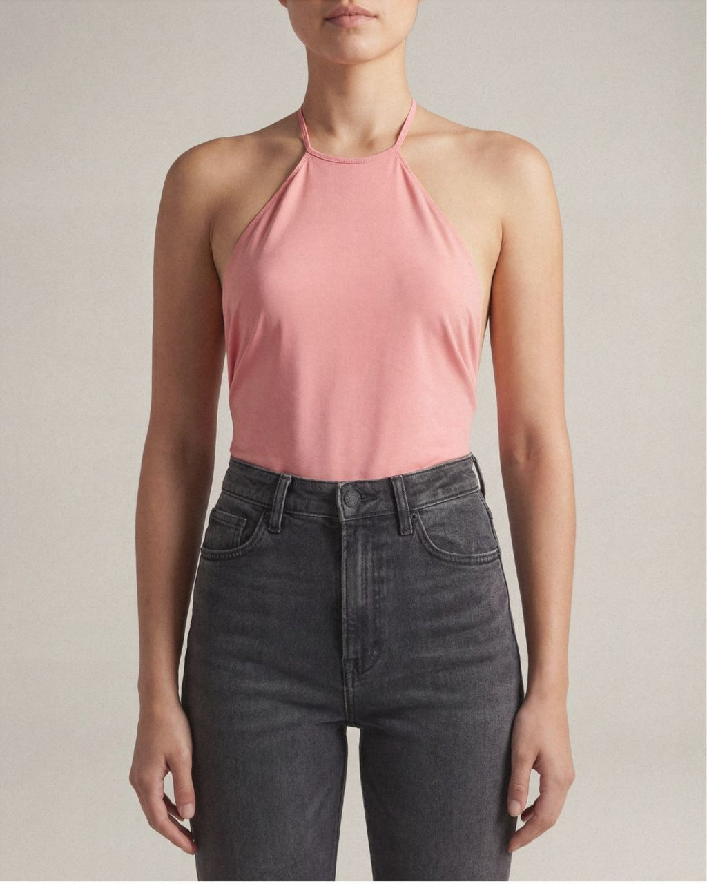 Person wearing a pink halter top and black jeans against a neutral background