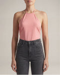Person wearing a pink halter top and black jeans against a neutral background
