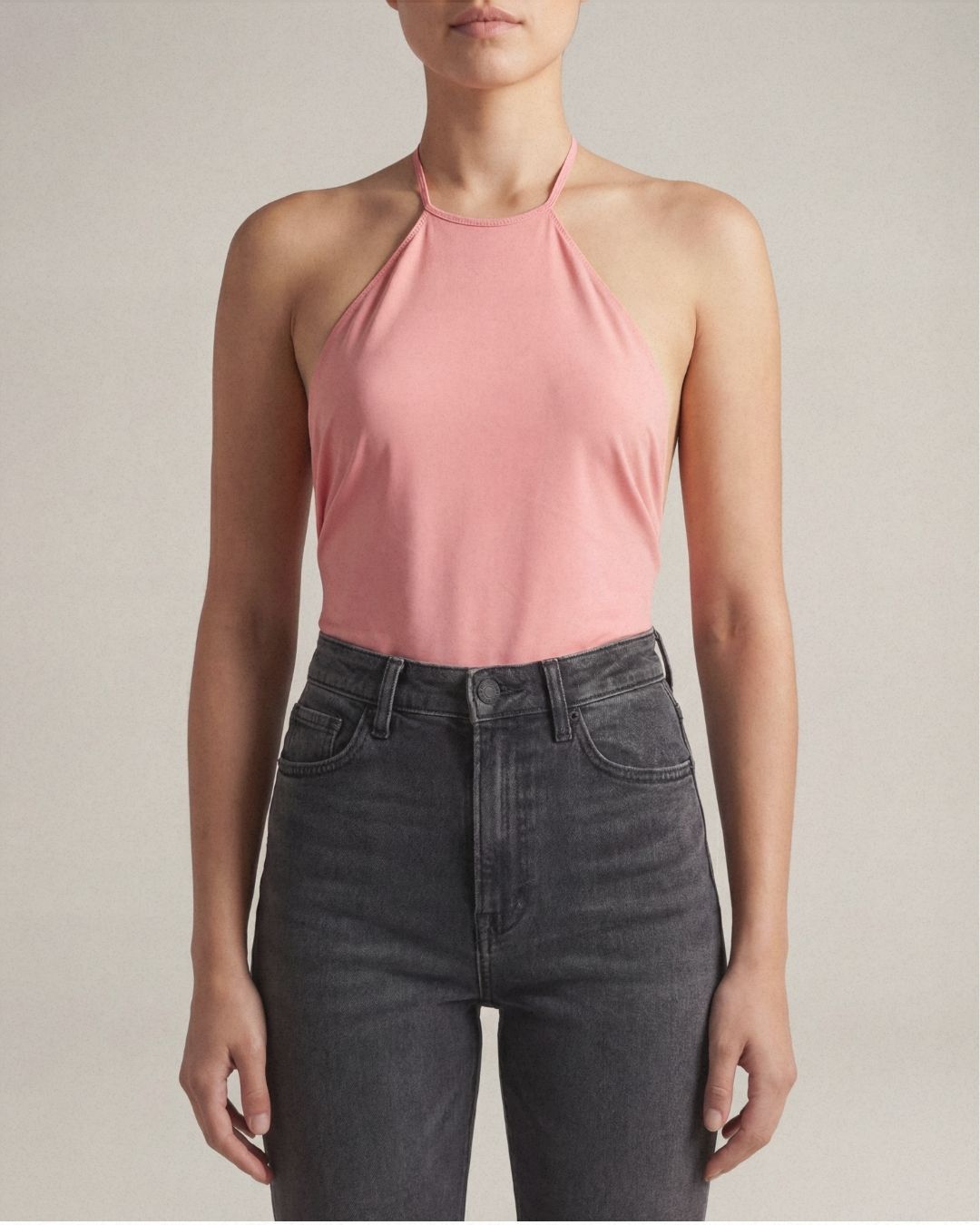 Person wearing a pink halter top and black jeans against a neutral background