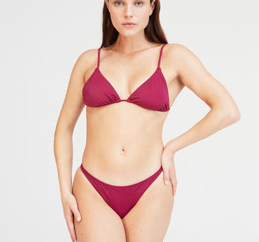 Model wearing Penelope Brazil Bikini Slip in grape purple, showcasing cheeky bikini briefs made from eco-friendly regenerated nylon.