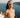 Woman in a beige tank top and headband standing in front of a scenic ocean view with sailboats.